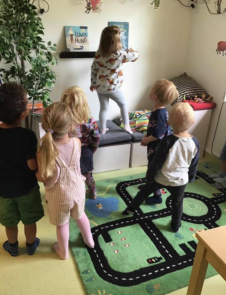 En grupp med barn står och tittar upp mot en bok på en hylla.