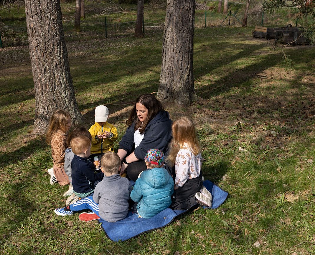 barn och pedagog sitter på en filt ute på marken